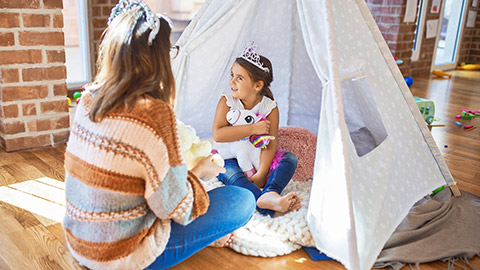 teacher and toddler wearing princess crown playing with unicorn doll inside tipi