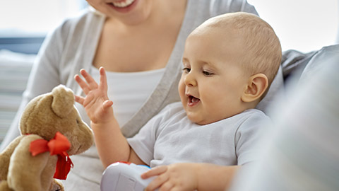 close up of happy smiling mother and little baby playing with teddy bear toy at home