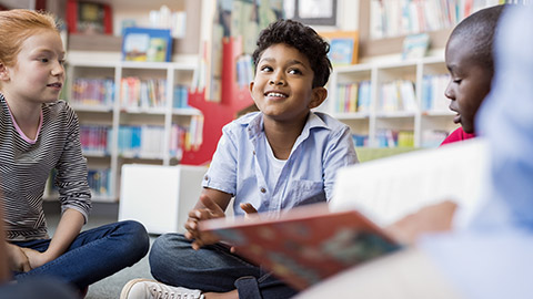 group of kids sitting on floor in circle around the teacher and listening a story