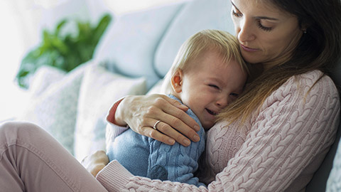 mother, holding her crying toddler boy, hugging him at home