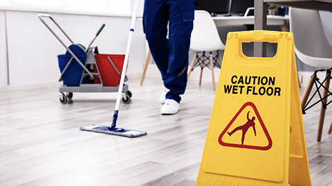 A person putting up a slippery floor sign while cleaning