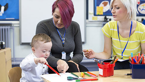 Nursery teacher sitting with a parent and her Down Syndrome son in the classroom