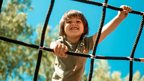 A child climbs up an alpine grid in a park on a playground on a hot summer day