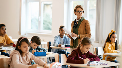 Mature teacher holding a class to group of school kids at primary school.