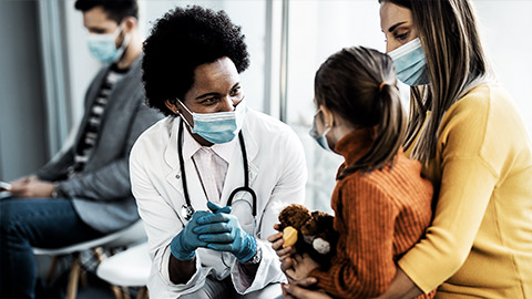 A medical professional wearing a mask attending to a child patient with her mother