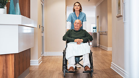 A worker wheeling a client around in an aged care facility