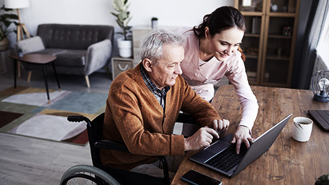 An elderly being helped by a carer operate a  laptop