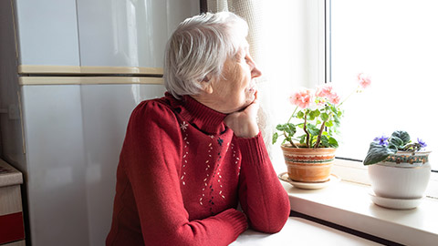 Old lonely woman sitting near the window at home