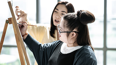 Autistic young woman gets help in painting by her guide