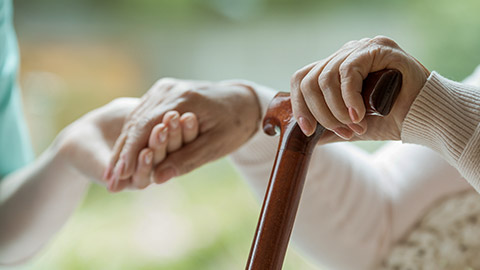 elder assisted by carer while using wooden cane