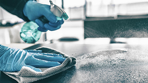 A gloved person cleaning and disinfecting a table top