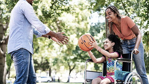 Girl in a wheelchair playing basketball with her family.