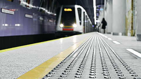 Metal tactile strips with an yellow line - for visually impaired (handicapped) and people with blindness - on an underground station, with a blurred arriving subway train and background