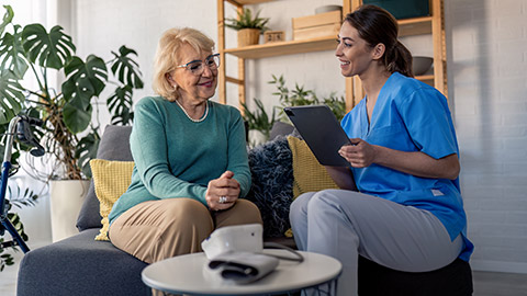 female home care worker using modern technology device, taking notes on digital tablet during home visit