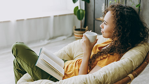 calm young woman wear t-shirt drink coffee read book sits in armchair