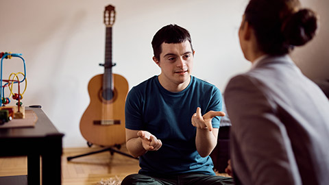 Young down syndrome man learning to count on his fingers with help of a tutor at home.