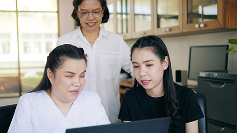 Asian women co-workers in workplace including person with blindness disability using laptop