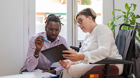 a businesswoman in a wheelchair with a disability looking at the digital tablet with her multiethnic business partner