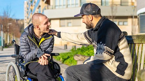 Disabled person in a wheelchair with a friend sitting having fun and talking