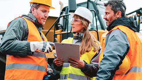 Three construction workers on a worksite discussing the details of a particular project