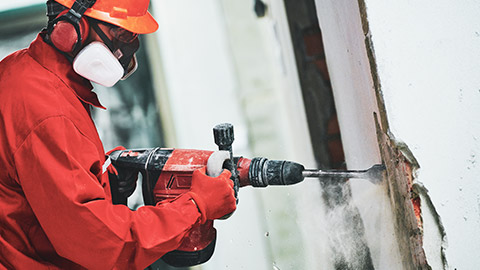 A construction worker wearing PPE demolishing a wall in an old building