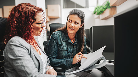 2 female coworkers at desk in office discussing contract