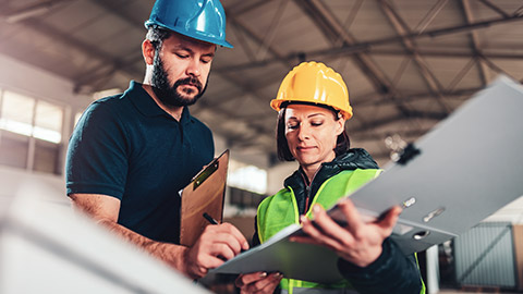 Coworkers on work site, 1 signing document being held by the other