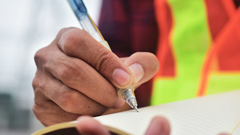 A close view of a construction worker's hand as they record data into a logbook