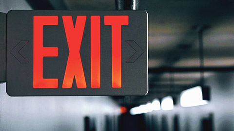 An illuminated exit sign in a corridor illuminted by emergency lighting