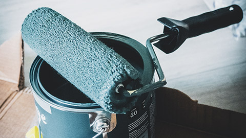 A paint roller sitting on top of an opened paint can