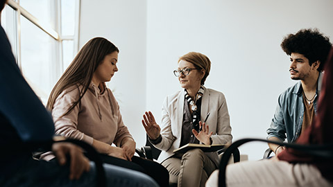 Mature mental health professional communicating with group of people during counseling at community center.