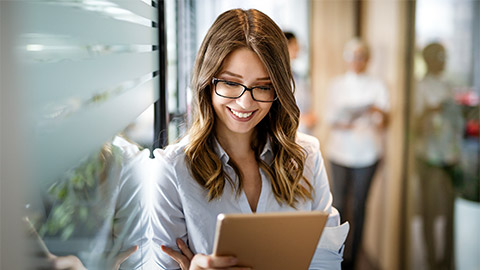 Attractive young businesswoman using a digital tablet while standing in front of windows in office