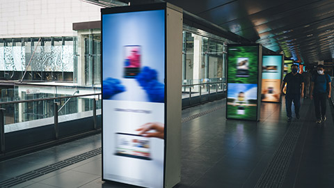 Group of people walking in public bridged walkway in station with blurred colorful digital signage advertisement board on passage in modern city at daylight