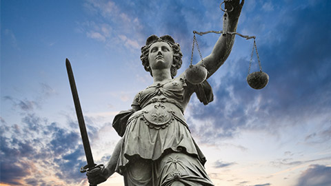 justice statue with sword and scale. cloudy sky in the background