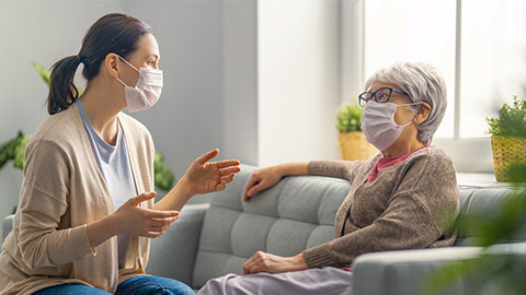 Beautiful mother and daughter are talking and smiling while sitting on couch at home.