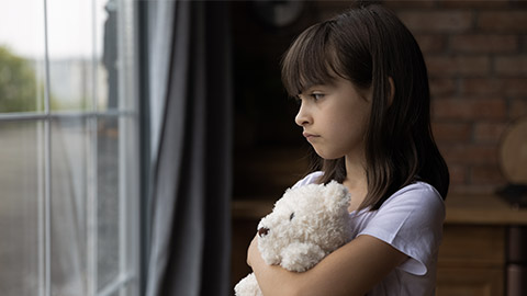 Close up lonely little girl hugging toy, looking out window