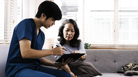 A nurse with a checklsit sits down with an in home patient during a visit