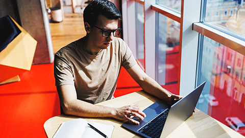 a young person reading on their laptop by the office window