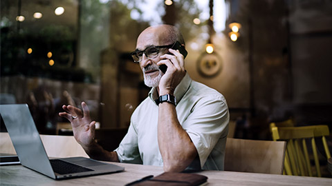 matured man working with computer talking on phone