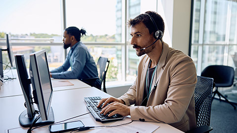 Male entrepreneur with headset working on a computer in the office.