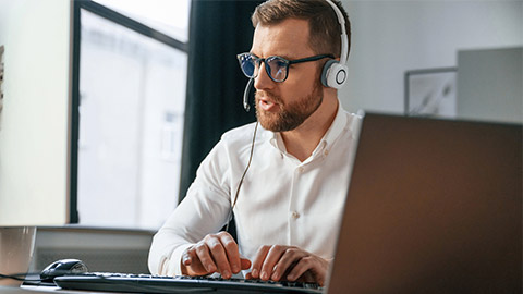 In headphones. Man in formal clothes is working in the modern office. Using computer.