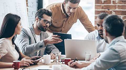 Group of five young people discuss something and gesturing while leaning to the table in office