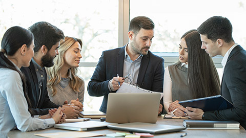 Group of diverse businesspeople going over paperwork together and working on a laptop at a table in office.