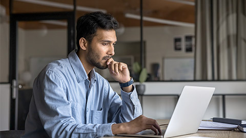 Pensive young Indian manager man working at laptop