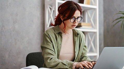 Young focused woman with red hair working with laptop while sitting in office