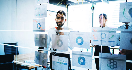 colleagues in formal wear developing work plan and goals in creative corporate office by writing and sticking papers with charts on glass wall