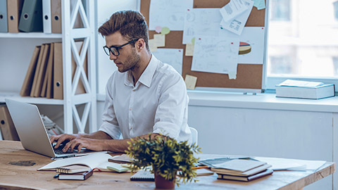 young man in glasses working with laptop while sitting at his working place