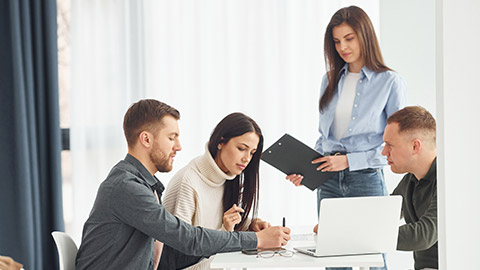 Four people works in the office by sitting by the table indoors.