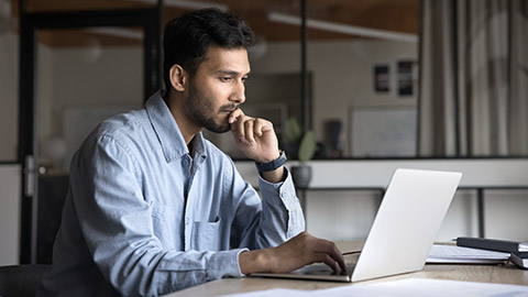 Pensive young Indian manager man working at laptop