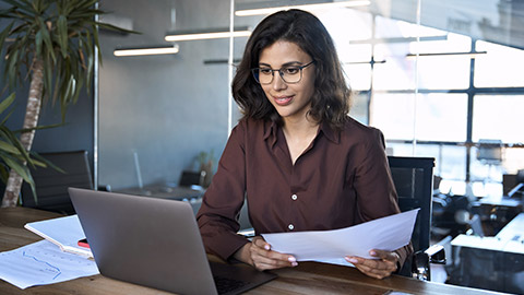 Focused latin hispanic young business woman working on laptop computer reading financial document report in office